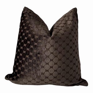 May include: A dark brown cushion with a velvety texture and a repeating pattern of large, raised circles. The cushion is square-shaped and appears soft. The design would suit a living room or bedroom.