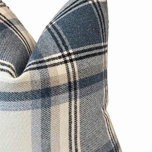 Pu&ograve; includere: Primo piano di un cuscino decorativo con un motivo a quadri blu, bianchi e neri. Il cuscino ha un aspetto morbido e strutturato, con il design a quadri che crea un'estetica classica e accogliente. &Egrave; un oggetto di arredamento per la casa.