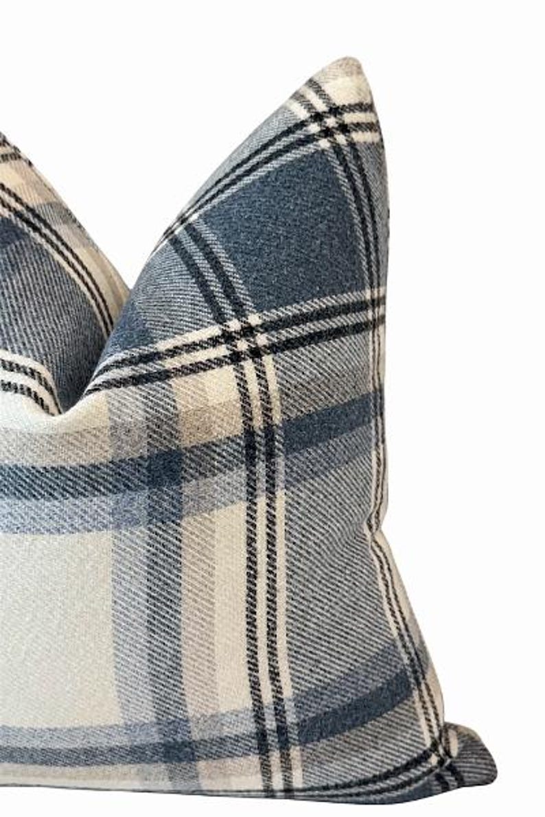 Pu&ograve; includere: Primo piano di un cuscino decorativo con un motivo a quadri blu, bianchi e neri. Il cuscino ha un aspetto morbido e strutturato, con il design a quadri che crea un'estetica classica e accogliente. &Egrave; un oggetto di arredamento per la casa.