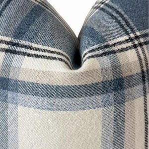 Pu&ograve; includere: Primo piano di un cuscino a quadri blu, bianco e beige. Il cuscino ha un aspetto morbido e strutturato con un classico motivo a quadri. La combinazione di colori &egrave; un mix di blu chiaro e scuro, bianco e beige, creando un'estetica accogliente e invitante.