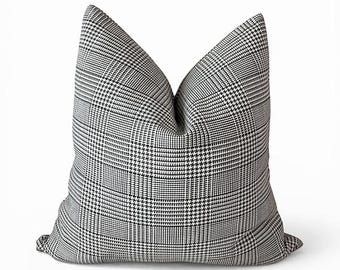 May include: A square throw pillow featuring a black and white houndstooth and glen plaid pattern. The fabric has a structured appearance with a visible crease at the top center, creating a soft, plump shape against a plain white background.