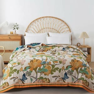 May include: A floral quilt with large yellow and green flowers, blue butterflies, and green leaves on a cream background. The quilt has an orange border with green stripes. It is on a bed with white pillows.