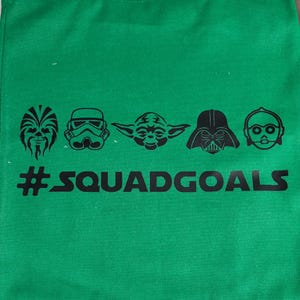May include: Green tote bag featuring black illustrations of Star Wars characters: Chewbacca, a Stormtrooper, Yoda, Darth Vader, and C-3PO. Below the characters is the text "#SQUADGOALS".