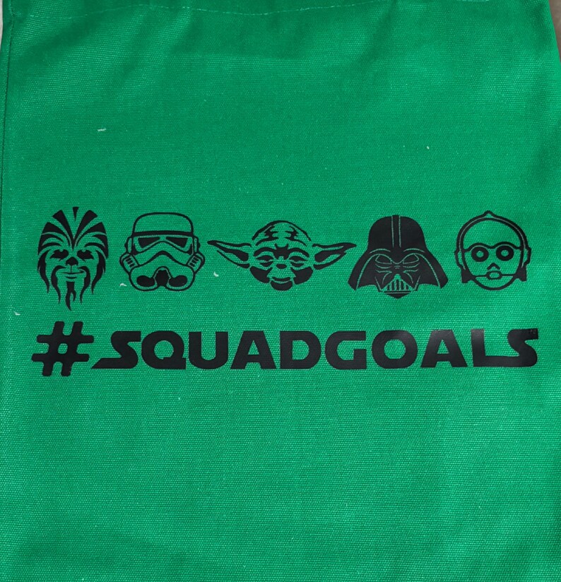May include: Green tote bag featuring black illustrations of Star Wars characters: Chewbacca, a Stormtrooper, Yoda, Darth Vader, and C-3PO. Below the characters is the text "#SQUADGOALS".