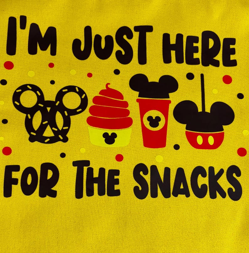 May include: Yellow canvas bag with the text "I'M JUST HERE FOR THE SNACKS" in black. The bag features illustrations of a pretzel, a cupcake, a coffee cup, and a Mickey Mouse-shaped balloon, all in black, red, and yellow.