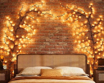 May include: A bedroom scene with a brick wall decorated with two branches of warm fairy lights. A bed with a woven headboard and pillows is in front of the wall. A nightstand and a clock are visible.