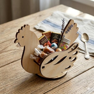 Könnte beinhalten: Ein hölzerner, huhnförmiger Korb gefüllt mit verschiedenen Süßigkeiten und Pralinen. Der Korb ist aus hellem Holz gefertigt und weist ausgeschnittene Details auf. Ein kleines Glas mit bunten Süßigkeiten und ein Zweig Lavendel sind ebenfalls enthalten.