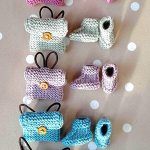 Peut inclure: Cinq ensembles d'articles tricotés miniatures, chacun composé d'un petit sac avec un bouton marron et d'une paire de chaussons assortis. Les ensembles sont disposés en colonne verticale, dans des tons rose, vert clair, lavande, bleu clair et bleu foncé.