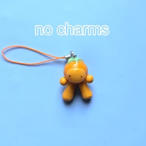 May include: An orange, humanoid-shaped charm with a light green top, featuring a smooth, glossy finish. It is attached to a thin orange cord loop. The text 'no charms' is printed in white above the object against a light blue background.