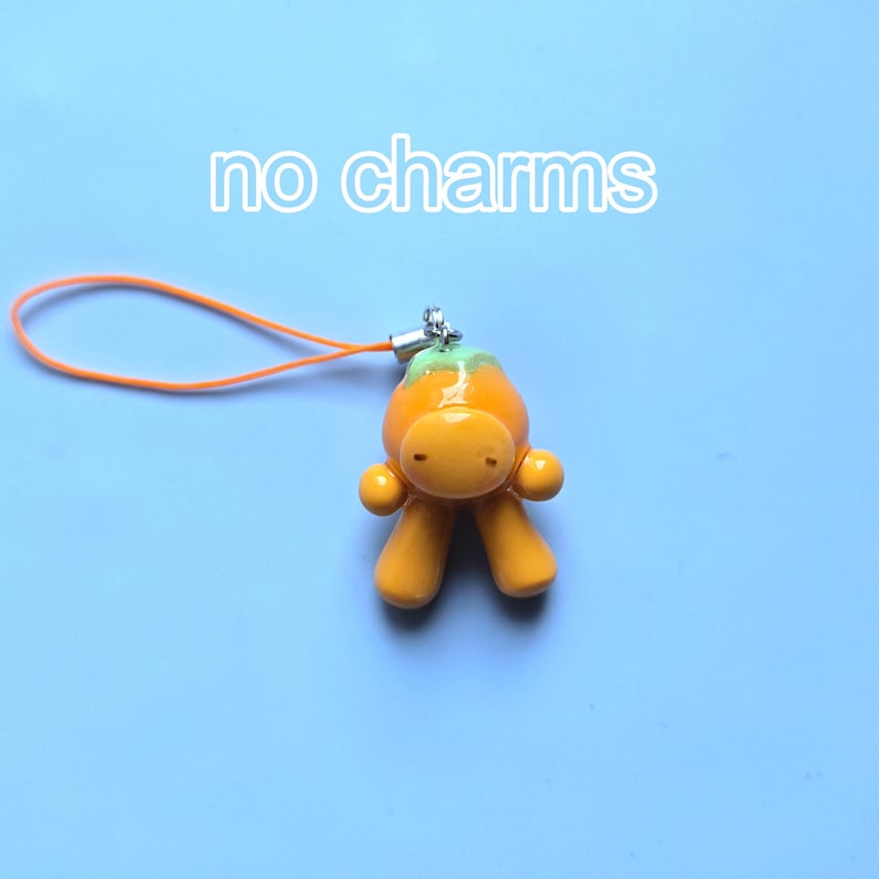 May include: An orange, humanoid-shaped charm with a light green top, featuring a smooth, glossy finish. It is attached to a thin orange cord loop. The text 'no charms' is printed in white above the object against a light blue background.