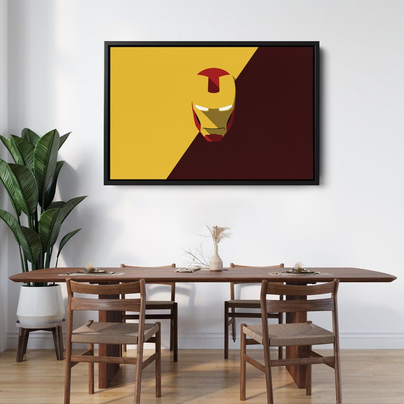 May include: Framed wall art featuring the Iron Man mask. The artwork has a yellow and maroon background with the Iron Man mask in the center. The artwork is displayed above a wooden dining table and chairs.