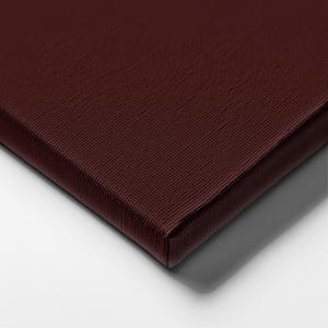 May include: Close-up of a burgundy canvas with a textured surface. The canvas is stretched over a wooden frame, with a visible corner and edge. The color is a deep, rich shade of red-brown.