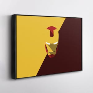 May include: Framed canvas art featuring a minimalist design of the Iron Man mask. The artwork is divided diagonally, with a yellow and maroon background. The mask is red and gold, with white eye slits.