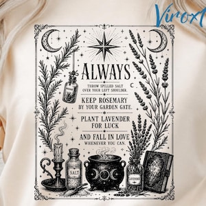 May include: A cream-colored t-shirt featuring a black ink illustration of a cauldron, a candle, jars labeled salt and lavender, and a book of spells. The text reads: ALWAYS THROW SPILLED SALT OVER YOUR LEFT SHOULDER. KEEP ROSEMARY BY YOUR GARDEN GATE. PLANT LAVENDER FOR LUCK AND FALL IN LOVE WHENEVER YOU CAN.