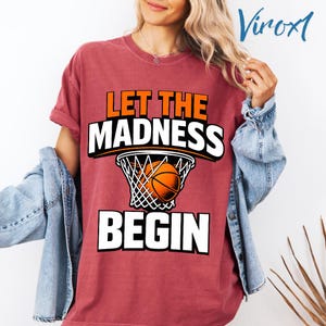 May include: A maroon t-shirt with the text "LET THE MADNESS BEGIN" in white and orange. The design includes a basketball going into a net. The shirt has rolled-up sleeves and is worn with a denim jacket.