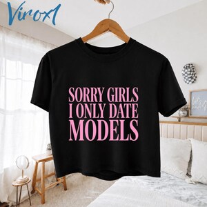 May include: Black crop top with the text "SORRY GIRLS I ONLY DATE MODELS" in pink. The shirt is hanging on a wooden hanger. The brand name "Viroxl" is in the upper left corner.