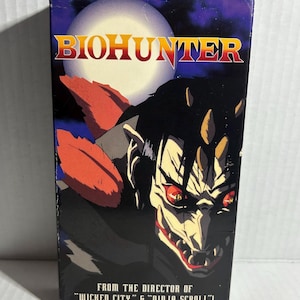 Può includere: Una videocassetta VHS del film d'animazione "Biohunter". La copertina presenta un personaggio demoniaco minaccioso con occhi rossi e denti affilati su uno sfondo blu scuro e viola. Il titolo "BIOHUNTER" è in lettere dorate. Il testo in basso recita "FROM THE DIRECTOR OF 'WICKED CITY' & 'NINJA SCROLL'!"