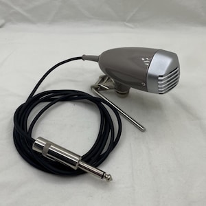 May include: A grey vintage microphone with a silver front grill and a black cable. The microphone is mounted on a silver stand and has a silver jack at the end of the cable. The cable is coiled.