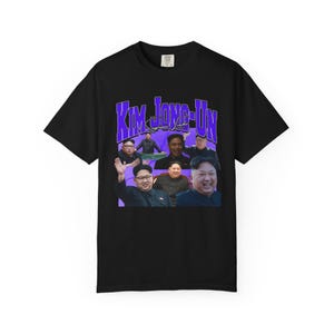 May include: Black t-shirt featuring a collage of images and the text "KIM JONG-UN" in purple. The shirt has a crew neck and short sleeves. The text "Supreme Leader" is also visible.