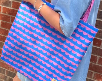 May include: A pink and blue tote bag with a repeating pattern of pink half-circles on a blue background. The bag has a pink handle and a yellow label that says "Happy Willow".