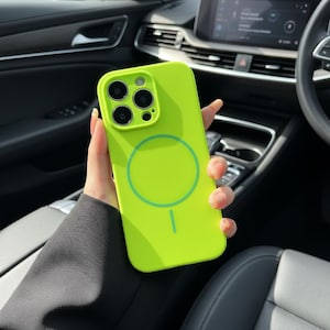 Puede incluir: Funda de teléfono verde neón brillante con un diseño circular y un recorte para la cámara. La funda se sostiene en una mano, mostrando su color vibrante y su diseño elegante. La funda está diseñada para un teléfono inteligente.