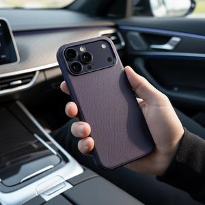 May include: A dark purple smartphone case with a textured surface. The case has a camera cutout with three lenses and a flash. The phone case is being held in a person's hand inside a car.