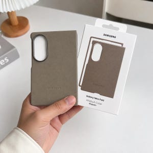 May include: A taupe Samsung Galaxy New Fold Kindsuit Case with a MagSafe compatible design. The case features a dark oval camera cutout and the Samsung logo embossed on the bottom. It is presented with its original white retail packaging.