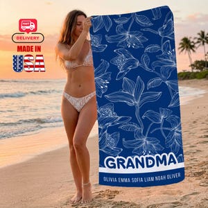 Puede incluir: Una toalla de playa azul con un estampado floral blanco y la palabra "GRANDMA" en blanco. Debajo están los nombres Olivia, Emma, Sofia, Liam, Noah y Oliver. Fabricado en EE. UU.