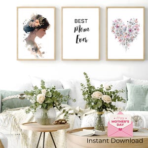 May include: Three framed art prints. One features a watercolor portrait of a woman with flowers in her hair. The second print says "BEST Mom Ever" in black text. The third print shows a heart made of flowers. The prints are in a living room setting.