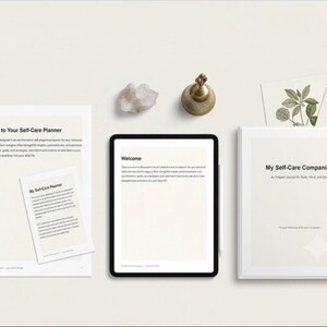 Könnte beinhalten: Ein Selbstpflege-Planer-Set mit einem gedruckten Dokument mit dem Titel Welcome to Your Self-Care Planner, einem Tablet mit einer Willkommensseite und einem Ordner mit dem Titel My Self-Care Companion. Eine kleine Messingglocke und ein Kristall.