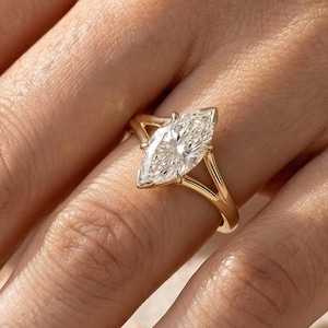 Könnte beinhalten: Ein goldener Ring mit einem Diamanten im Marquiseschliff. Der Ring hat ein geteiltes Schaftdesign. Der Diamant ist in einer Krappenfassung gefasst und scheint klar zu sein. Der Ring befindet sich am Finger einer Person.