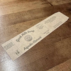 May include: A rectangular, tan Goat Milk Soap label with the words "Goat Milk Soap" and "Aquatic Element" printed on it. The label also includes the text "Made with only 6X total ingredients for moisturizing and nourishing skin care."