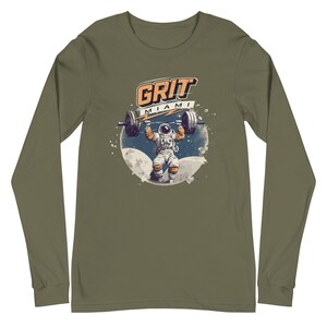 May include: Olive green long-sleeve shirt featuring a graphic of an astronaut lifting a barbell with the text "GRIT MIAMI". The astronaut is set against a backdrop of a moon and stars. The shirt is made of a soft material.