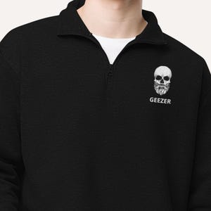 May include: Black quarter-zip sweatshirt with a white skull with a beard graphic and the word "Geezer" printed below it.
