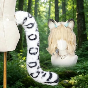 May include: A white and black spotted faux fur tail attached to a mannequin. A mannequin head with blonde wavy hair and cat ears with blue accents is also visible. The background is a blurred forest scene.