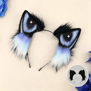 Puede incluir: Una diadema negra con dos orejas de animal de piel sintética. Las orejas tienen un patrón degradado que va del negro en las puntas al morado y blanco en la base. Cada oreja presenta un pequeño emblema de estrella blanca de cuatro puntas.