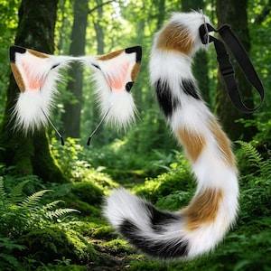 May include: A cat ear headband and a matching tail set. The ears are white with brown and black accents, and pink inner ears. The tail is a mix of white, brown, and black faux fur, with a black strap for attachment.