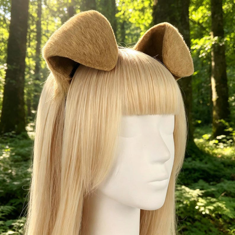 May include: A tan-colored headband with two plush, upright dog ears. The ears are a lighter shade of brown and have a soft, textured appearance. The headband is worn on a mannequin head with long, straight blonde hair.