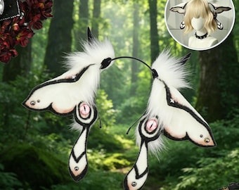 May include: A pair of white and black butterfly-shaped hair accessories with fluffy white fur and pink eye details. The accessories are attached to a black headband. The image also includes a smaller inset image of the accessories on a mannequin.