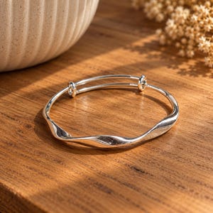 925 sterling silver Mobius bangle bracelet for women, with a smooth band that twists into a continuous infinity loop. The polished silver has a bright, reflective finish and a clean, minimalist look. The adjustable design gives a comfortable fit on most wrists, making it easy to wear every day. It layers well with other bracelets or stands out beautifully on its own. An elegant silver bangle for weddings, bridal looks or a meaningful gift symbolising everlasting love.