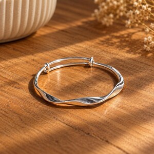 925 sterling silver Mobius bangle bracelet for women, with a smooth band that twists into a continuous infinity loop. The polished silver has a bright, reflective finish and a clean, minimalist look. The adjustable design gives a comfortable fit on most wrists, making it easy to wear every day. It layers well with other bracelets or stands out beautifully on its own. An elegant silver bangle for weddings, bridal looks or a meaningful gift symbolising everlasting love.