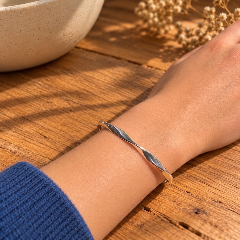 925 sterling silver Mobius bangle bracelet for women, with a smooth band that twists into a continuous infinity loop. The polished silver has a bright, reflective finish and a clean, minimalist look. The adjustable design gives a comfortable fit on most wrists, making it easy to wear every day. It layers well with other bracelets or stands out beautifully on its own. An elegant silver bangle for weddings, bridal looks or a meaningful gift symbolising everlasting love.