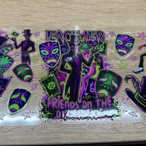May include: A clear transfer sheet featuring a purple and green graphic design with a central figure in a top hat, surrounded by theatrical masks, playing cards, and skull-adorned hats. The text reads "FACILIER" and "FRIENDS ON THE OTHER SIDE".