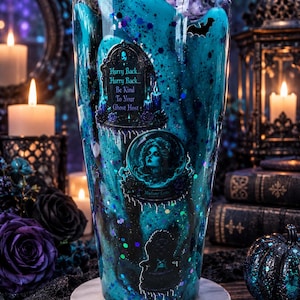 May include: A clear tumbler filled with a swirling teal and black liquid containing glitter. The exterior features decals of a tombstone with the text "Hurry Back... Hurry Back... Be Kind To Your Ghost Host", a portrait of Madame Leota, and a bat.