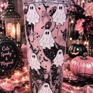 May include: A clear double-walled tumbler filled with pink liquid and black glitter, featuring a repeating pattern of white ghosts with pink bows and small black bats. The ghosts have black oval eyes and are decorated with pink bow prints.