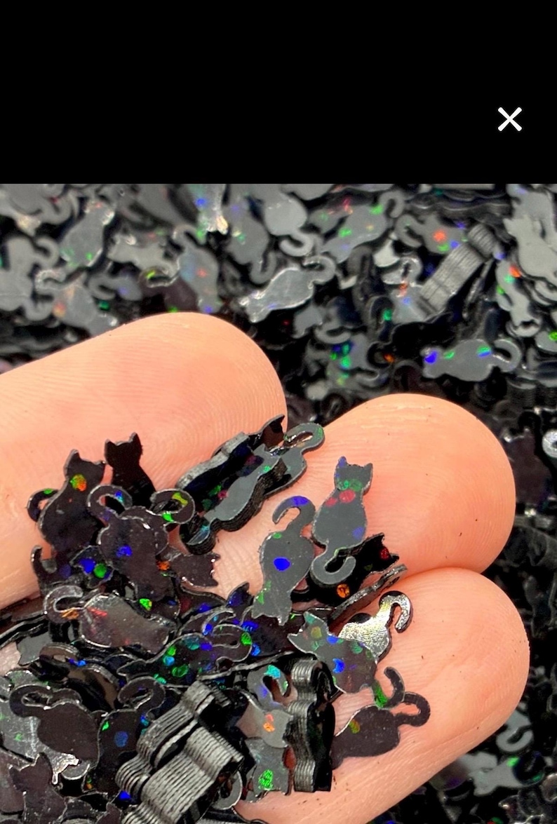 May include: A collection of small, black cat-shaped sequins featuring a holographic finish that reflects multi-colored light. Each individual piece is shaped like a sitting cat with a curved tail, designed for decorative craft applications.