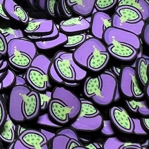 May include: A collection of small, flat, purple-colored charms shaped like halved fruits. Each piece features a light green interior with dark green seeds and a black outline, creating a uniform, repeating pattern of identical fruit-themed items.