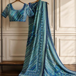 May include: A blue and teal saree with a matching short-sleeved blouse, both featuring intricate geometric patterns, diagonal stripes, and small reflective embellishments throughout the fabric, displayed on wooden hangers on a metal rack.