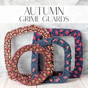 Peut inclure: Trois housses de jante décoratives avec des motifs d'automne. L'une présente des champignons, une autre des fraises rouges et la troisième des feuilles. Le texte "AUTUMN GRIME GUARDS" est affiché au-dessus des housses.