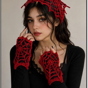 Puede incluir: Un pañuelo de crochet rojo y guantes sin dedos a juego, ambos con un intrincado patrón de telaraña. El pañuelo tiene forma triangular y los guantes cubren el dorso de las manos con un delicado diseño de red calada.